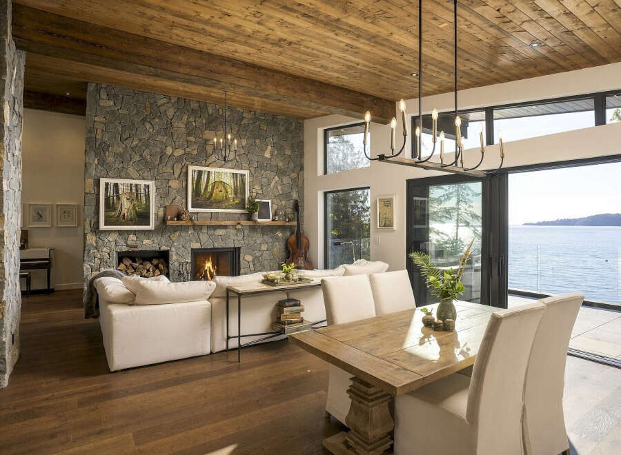 Experience luxurious waterfront living in this stunning home featuring a grand stone fireplace and a rustic wood-paneled ceiling.