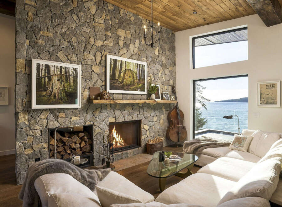 Experience breathtaking ocean views from this stunning living room, featuring a grand stone fireplace and a cozy seating area perfect for relaxation.
