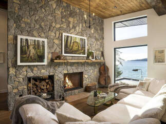 Experience breathtaking ocean views from this stunning living room, featuring a grand stone fireplace and a cozy seating area perfect for relaxation.