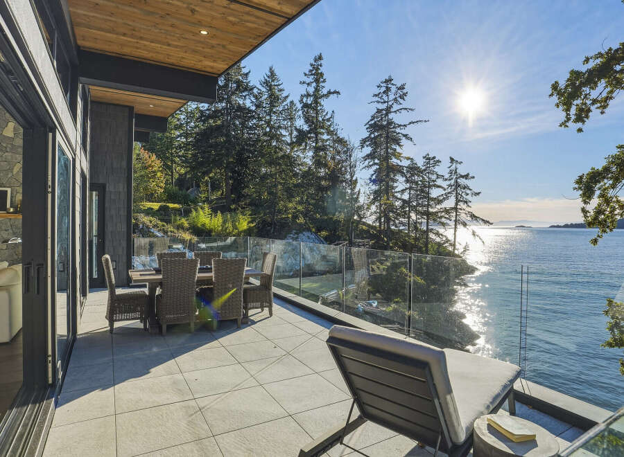 Experience luxurious waterfront living with this stunning patio, featuring a dining set and lounge chair perfect for enjoying the breathtaking ocean views.
