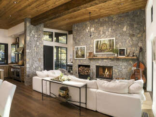 Experience rustic luxury in this stunning living space, featuring a grand stone fireplace and a warm, wood-paneled ceiling.