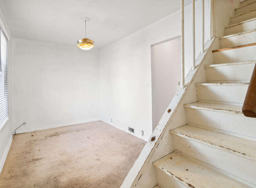 This interior shot showcases a room with a beige carpet and white walls, featuring a prominent wooden staircase on the right.