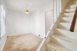 This interior shot showcases a room with a beige carpet and white walls, featuring a prominent wooden staircase on the right.