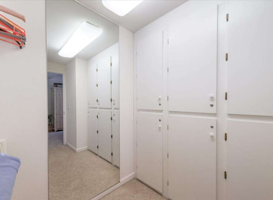This hallway features a full-length mirror that reflects a row of white cabinets, offering ample storage space.