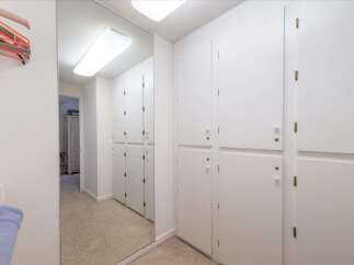 This hallway features a full-length mirror that reflects a row of white cabinets, offering ample storage space.