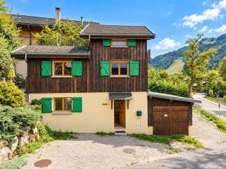 Charming wooden chalet nestled in a picturesque mountain landscape, featuring vibrant green shutters and a welcoming yellow facade.