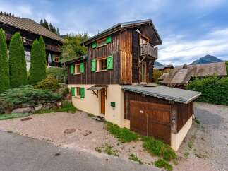 Charming wooden chalet nestled in a serene mountain landscape, featuring vibrant green shutters and a rustic balcony.