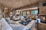 Experience luxurious mountain living in this stunning chalet-style living room, featuring a warm and inviting ambiance with exposed wooden beams and a crackling fireplace.