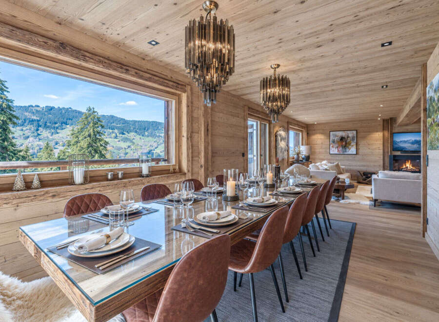 Experience luxurious mountain living in this stunning dining room, featuring a grand wooden table set for a feast and surrounded by elegant leather chairs.