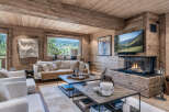 Experience luxurious mountain living in this stunning chalet, featuring a cozy living room with a modern fireplace and a large window offering breathtaking panoramic views of the rolling hills and lush greenery.