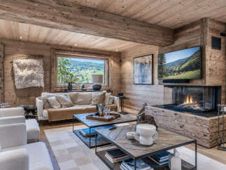 Experience luxurious mountain living in this stunning chalet, featuring a cozy living room with a modern fireplace and a large window offering breathtaking panoramic views of the rolling hills and lush greenery.