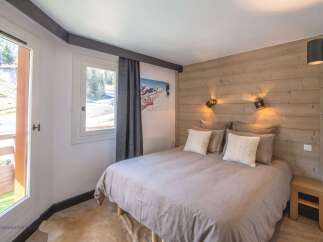 Experience cozy mountain living in this charming bedroom, featuring a comfortable bed adorned with plush pillows and a rustic wooden accent wall.