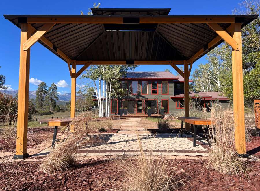 Enjoy outdoor living under this elegant wooden gazebo, featuring a dark metal roof and built-in seating.