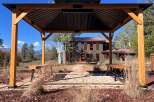Enjoy outdoor living under this elegant wooden gazebo, featuring a dark metal roof and built-in seating.