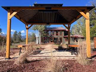 Enjoy outdoor living under this elegant wooden gazebo, featuring a dark metal roof and built-in seating.