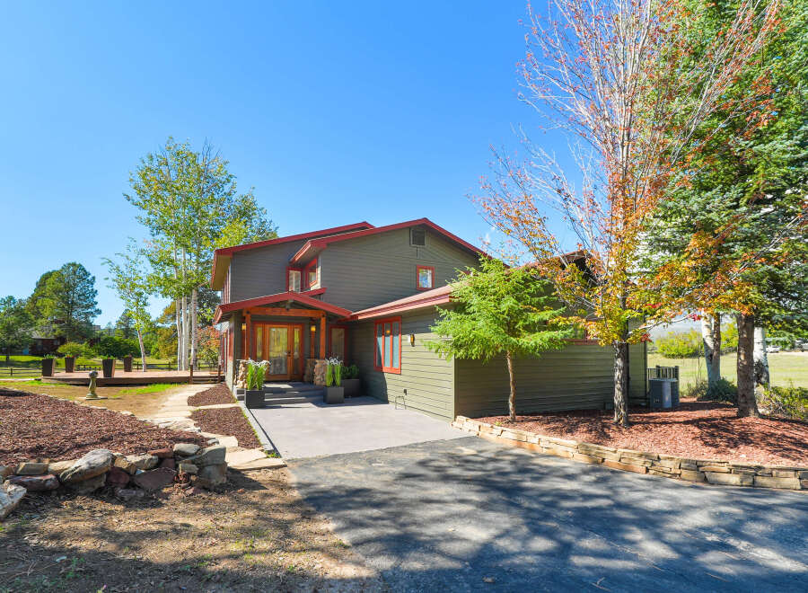 This charming two-story home features a welcoming covered porch with double wooden doors, stone accents, and large planters.