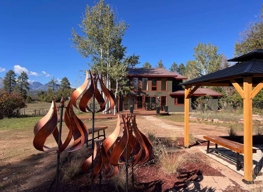 Experience serene mountain living in this stunning property, featuring a modern home with a dark green exterior and vibrant red trim, complemented by a spacious wooden deck.
