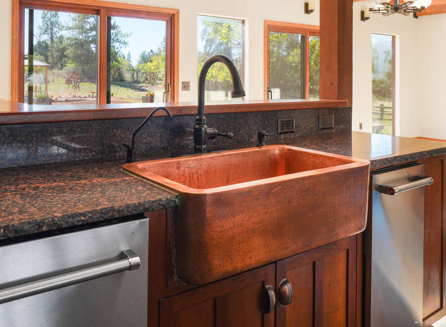 This kitchen boasts a stunning copper farmhouse sink, complemented by dark granite countertops and rich wooden cabinetry.