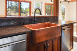 This kitchen boasts a stunning copper farmhouse sink, complemented by dark granite countertops and rich wooden cabinetry.