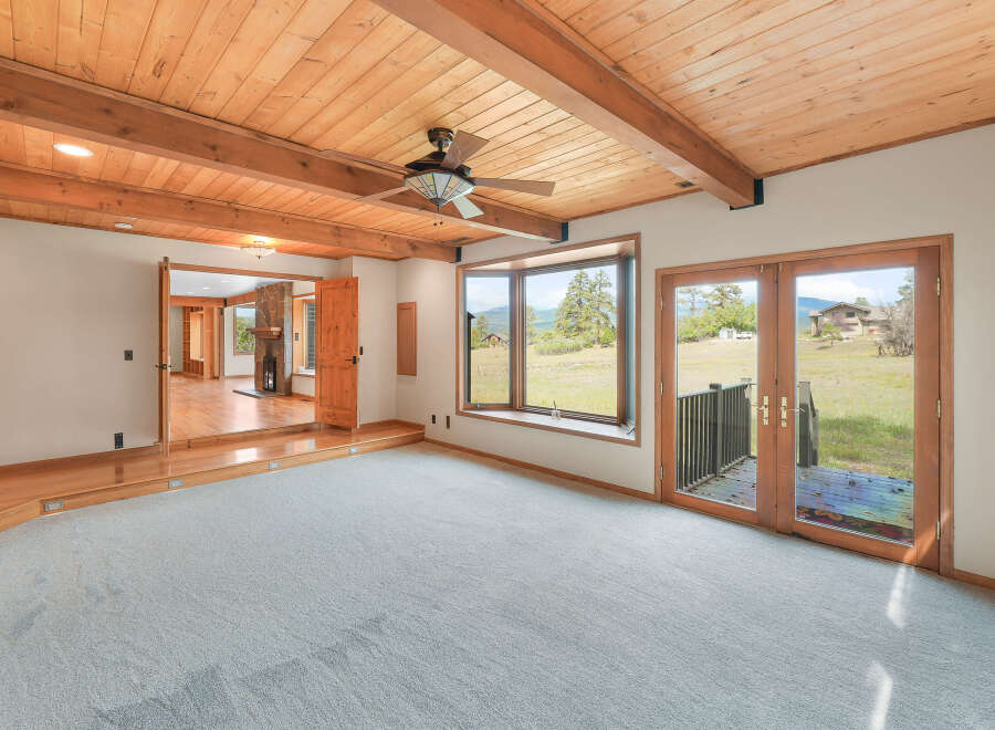 Experience breathtaking mountain views from this spacious living area, featuring a vaulted wood-beamed ceiling and a cozy fireplace visible through an open doorway.