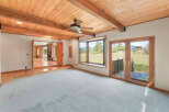 Experience breathtaking mountain views from this spacious living area, featuring a vaulted wood-beamed ceiling and a cozy fireplace visible through an open doorway.