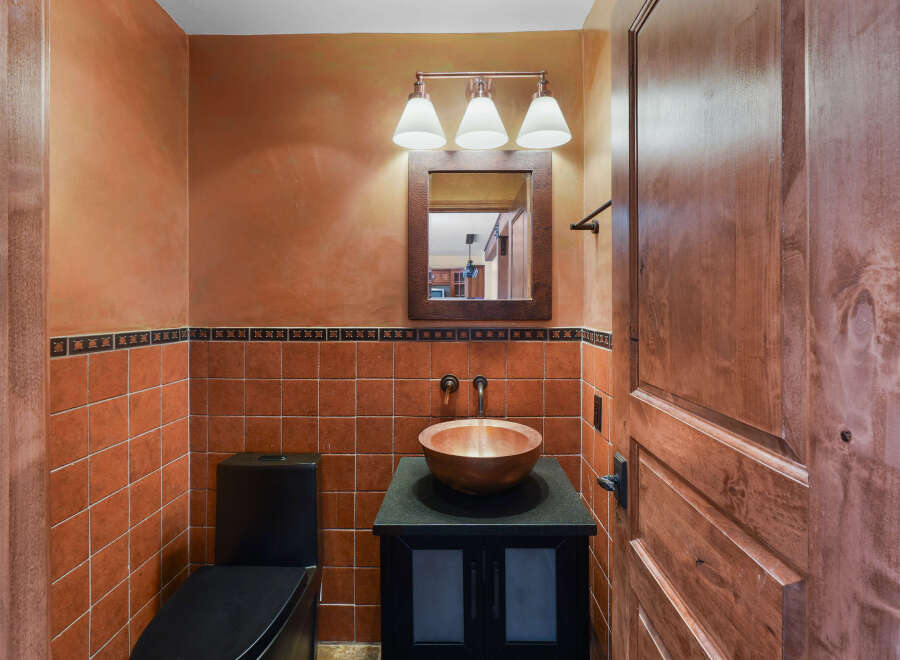 This powder room boasts a warm and inviting ambiance with its terracotta tiled walls and rich wooden accents.