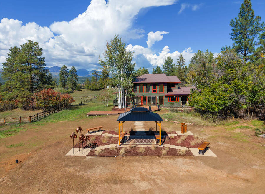 Experience serene mountain living in this stunning property, featuring a spacious green home with a metal roof and large windows offering breathtaking views.
