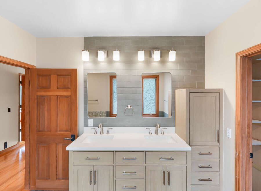 This modern bathroom features a spacious double vanity with sleek cabinetry and brushed nickel fixtures, complemented by a tiled backsplash and a contemporary light fixture.