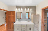 This modern bathroom features a spacious double vanity with sleek cabinetry and brushed nickel fixtures, complemented by a tiled backsplash and a contemporary light fixture.