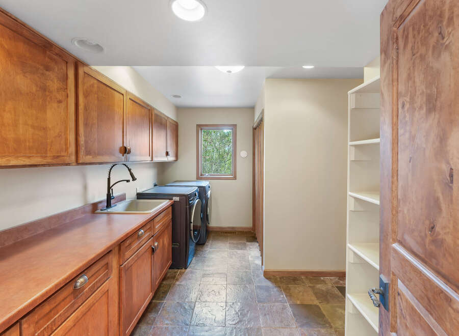 This spacious laundry room boasts ample storage with custom wooden cabinetry and open shelving.