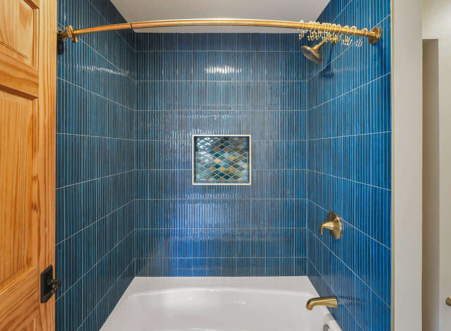 This modern bathroom features a stunning shower with vertical, deep blue tilework and a decorative mosaic accent.