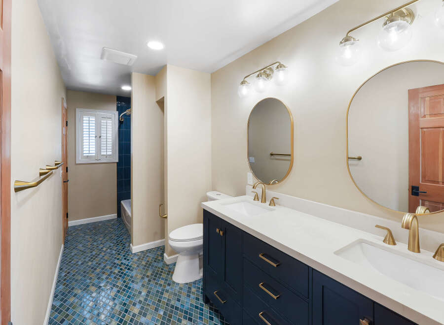 This modern bathroom features a deep navy vanity with brass hardware, complemented by a white quartz countertop and dual sinks.