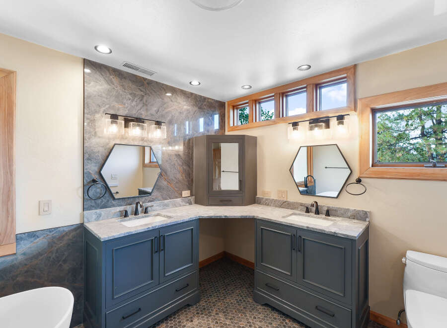 This luxurious bathroom features a double vanity with marble countertops and dark gray cabinetry, complemented by hexagonal mirrors and modern light fixtures.