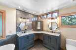 This luxurious bathroom features a double vanity with marble countertops and dark gray cabinetry, complemented by hexagonal mirrors and modern light fixtures.