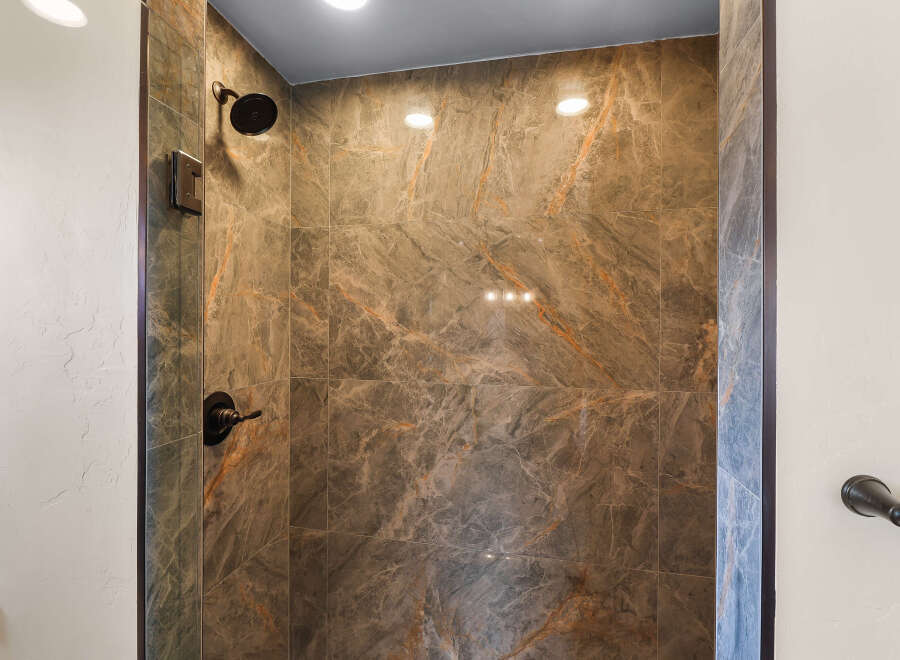 Step into a luxurious shower experience with stunning marble-look tiles in rich brown and orange tones.