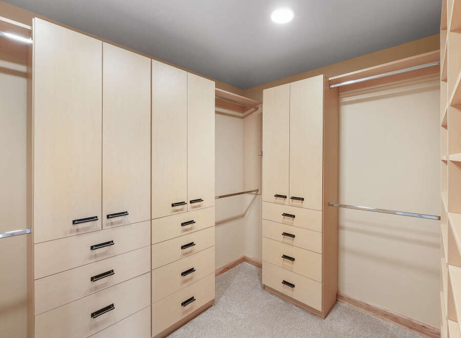 This spacious walk-in closet features custom light wood cabinetry with sleek black hardware, offering ample storage for your wardrobe.