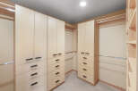 This spacious walk-in closet features custom light wood cabinetry with sleek black hardware, offering ample storage for your wardrobe.