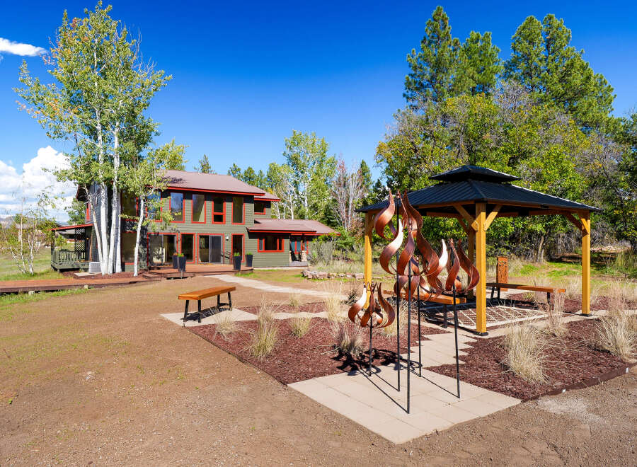 Discover this stunning property featuring a modern two-story home with a distinctive green exterior and red trim, complemented by a spacious wooden deck and a charming gazebo.