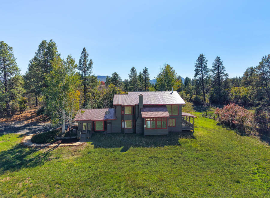 Nestled amidst a serene forest landscape, this multi-story home offers a unique architectural style with its dark siding and contrasting red window frames.