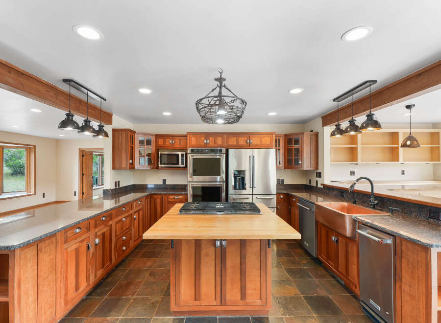 This spacious kitchen boasts custom cherry wood cabinetry, granite countertops, and a large butcher block island with a gas range.