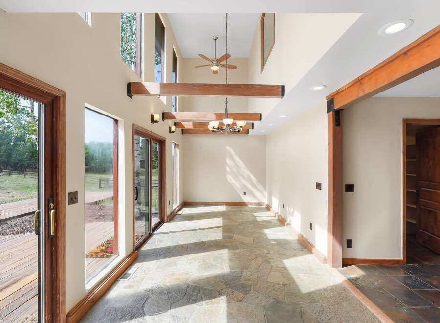 This spacious sunroom features a soaring vaulted ceiling with exposed wooden beams and a ceiling fan, complemented by a modern chandelier.