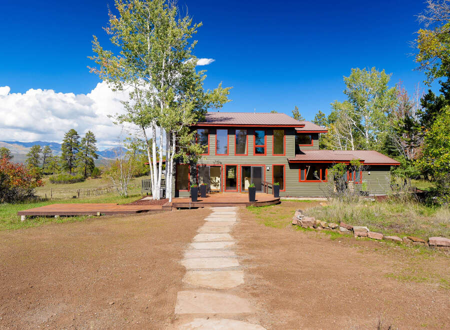 Experience the beauty of nature from this stunning home, featuring a spacious wooden deck perfect for outdoor entertaining and a charming stone pathway leading to the entrance.