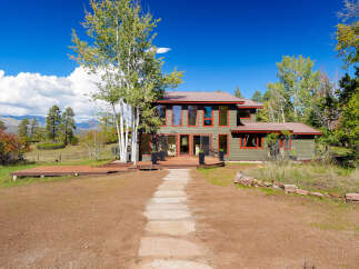 Experience the beauty of nature from this stunning home, featuring a spacious wooden deck perfect for outdoor entertaining and a charming stone pathway leading to the entrance.