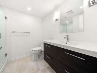 This modern bathroom features a sleek dark wood vanity with ample drawer storage, complemented by a spacious white countertop and a minimalist faucet.