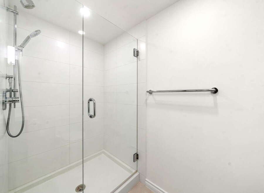 Experience modern luxury in this pristine bathroom, featuring a sleek glass-enclosed shower with a rainfall showerhead and a convenient handheld wand.