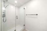 Experience modern luxury in this pristine bathroom, featuring a sleek glass-enclosed shower with a rainfall showerhead and a convenient handheld wand.