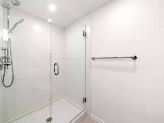 Experience modern luxury in this pristine bathroom, featuring a sleek glass-enclosed shower with a rainfall showerhead and a convenient handheld wand.