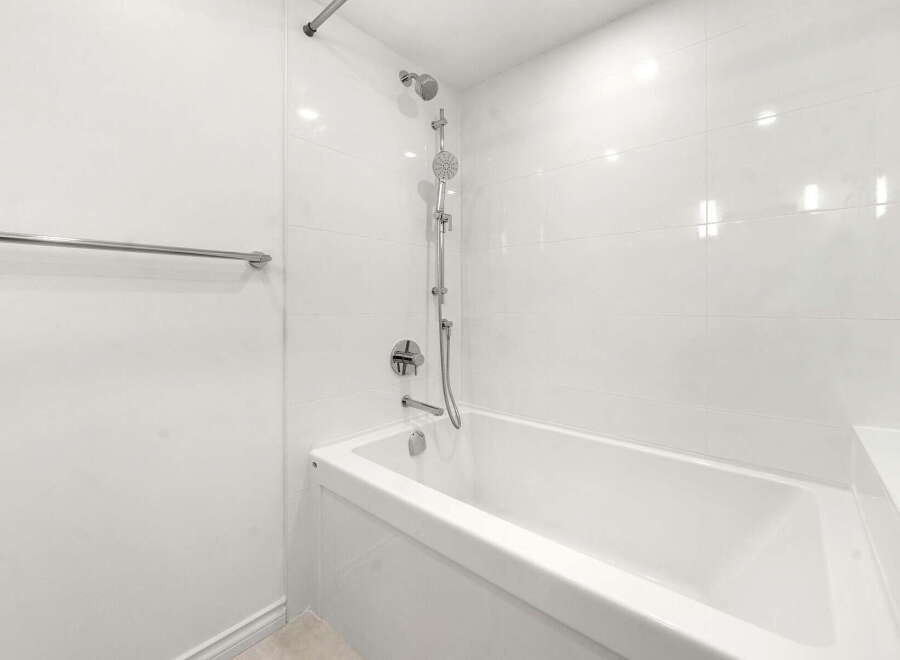 Experience modern comfort in this pristine bathroom, featuring a sleek white bathtub and a dual showerhead system for a luxurious bathing experience.