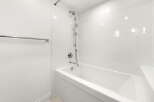 Experience modern comfort in this pristine bathroom, featuring a sleek white bathtub and a dual showerhead system for a luxurious bathing experience.