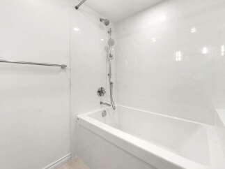 Experience modern comfort in this pristine bathroom, featuring a sleek white bathtub and a dual showerhead system for a luxurious bathing experience.